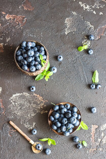 Bleuets fraîchement cueillis dans un bol en bois. Myrtilles fraîches et juteuses à la menthe sur une surface de pierre sombre. Concept pour une alimentation saine et la nutrition.