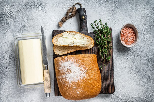 Bloc de beurre et tranches de pain grillé sur une planche de bois avec des herbes. Table blanche. Vue de dessus.