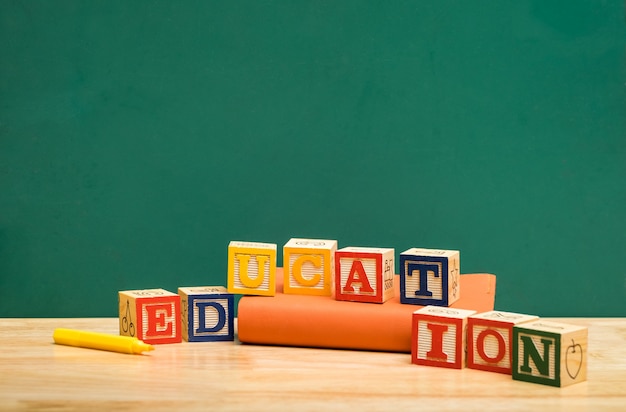 Bloc de bois mot éducation coloré sur le livre avec un stylo sur la table en bois avec tableau noir vert