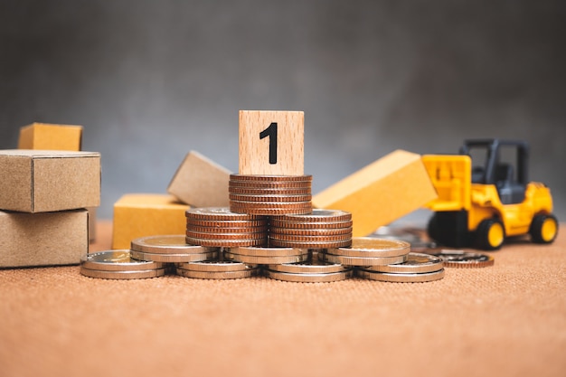 Bloc de bois numéro un sur pile de pièces de monnaie avec boîtes en carton et véhicule pour chariot élévateur