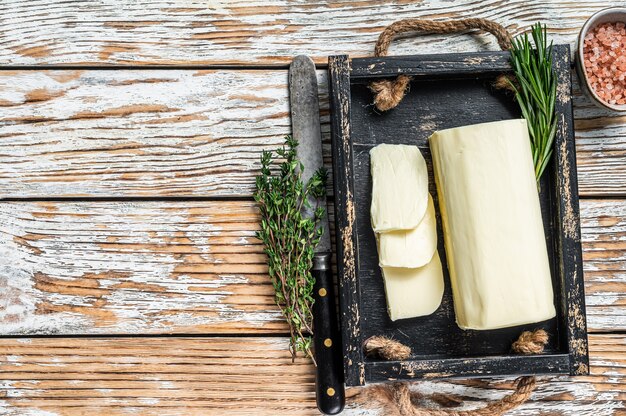 Bloc de margarine au beurre dans un plateau en bois avec des herbes. Fond en bois blanc. Vue de dessus. Espace de copie.