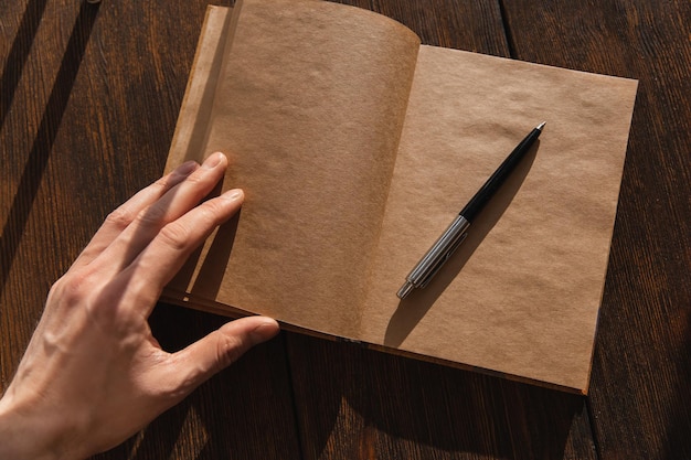 Le bloc-notes artisanal avec un stylo sur un fond en bois est ouvert par une main masculine