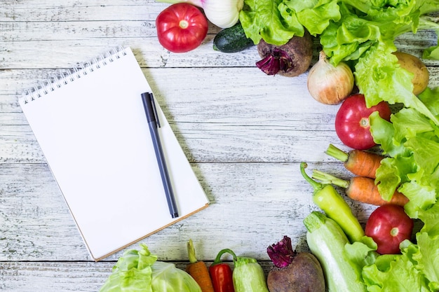 Bloc-notes blanc vierge de bordure de légumes juteux frais avec espace de copie et stylo sur la vue de dessus de fond en bois blanc