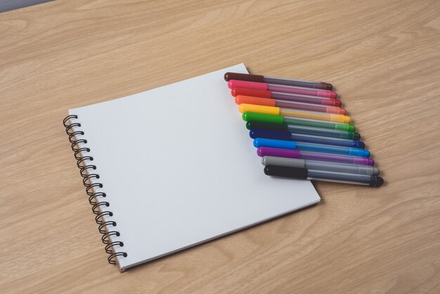 Bloc-notes ou cahier avec de nombreux stylos colorés sur une table en bois brun