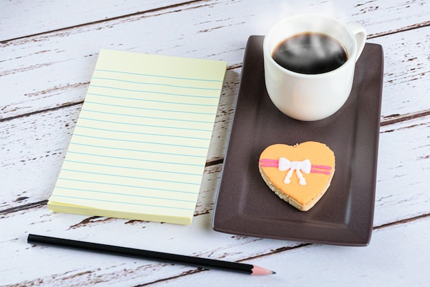 Bloc-notes à côté d'une tasse de café, d'un crayon et d'un biscuit.