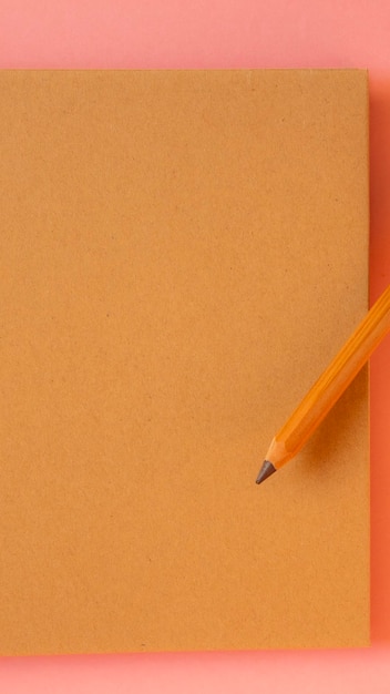 Bloc-notes avec un crayon sur la couverture sur fond rose clair