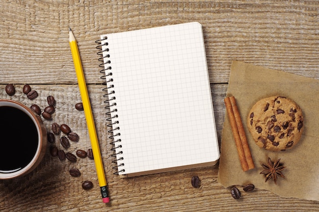 Bloc-notes, crayon et tasse à café ouverts sur une vieille table en bois. Vue de dessus