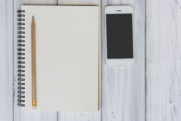 Bloc-notes, crayon et téléphone portable sur fond de table en bois blanc, concept d&#39;espace de travail