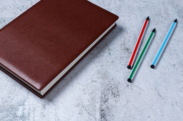 Bloc-notes en cuir rouge avec des stylos colorés sur fond de béton gris.