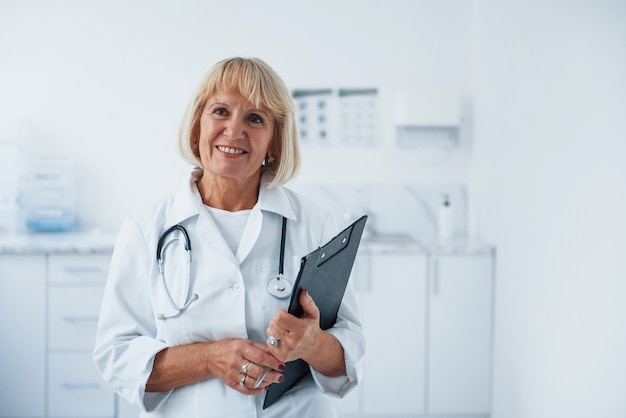 Avec bloc-notes dans les mains. Portrait d'un médecin senior en uniforme blanc qui se trouve dans la clinique.