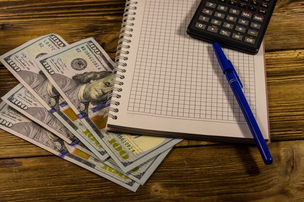 Bloc-notes avec dollars, stylo et calculatrice sur un bureau en bois. Notion financière