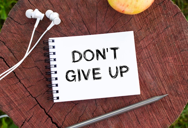 Photo un bloc-notes, des écouteurs, un crayon et une pomme reposent sur une souche en bois. sur la page du cahier, le texte est dont give up.