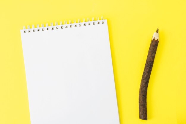 Bloc-notes avec une feuille blanche près d'un stylo en bois écologique sur fond jaune. Concept de Pâques