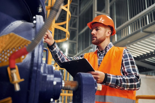 Avec bloc-notes Ouvrier du bâtiment en uniforme est dans l'usine