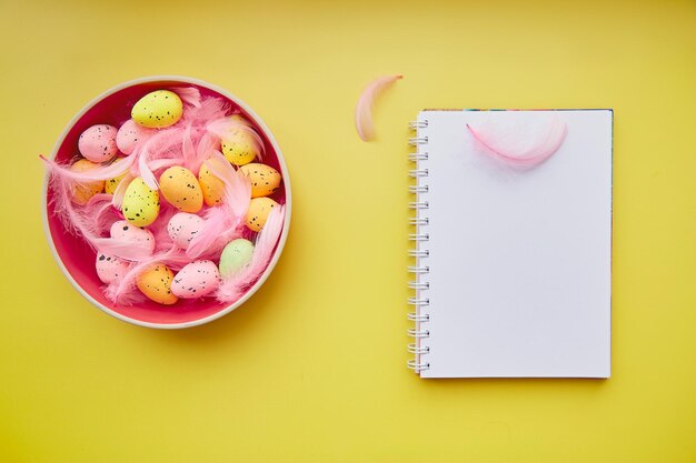 Bloc-notes de Pâques minimaliste maquette sur fond jaune. Bol rose - oeufs colorés et plumes roses