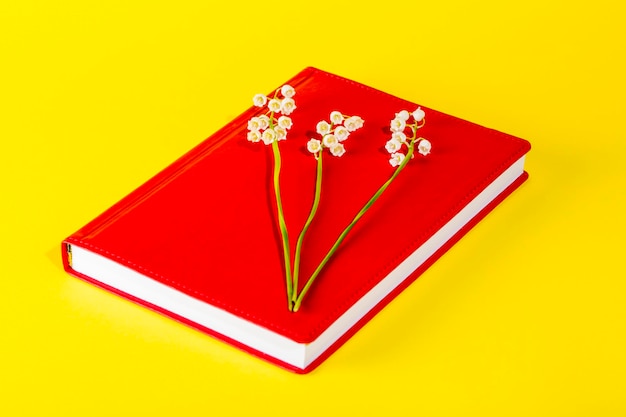 Bloc-notes rouge avec des fleurs de muguet sur fond jaune