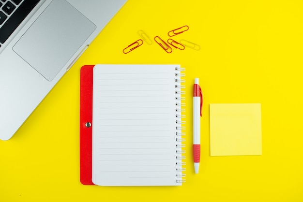 Bloc-notes rouge, stylo, clips colorés et ordinateur portable sur jaune