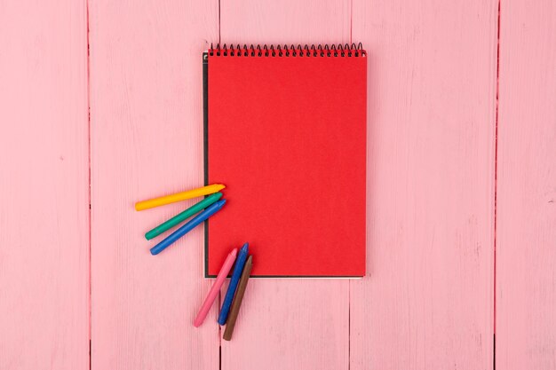 Bloc-notes rouge vierge et crayons sur table en bois rose