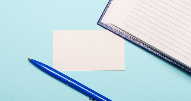 Photo bloc-notes, stylo blanc et carte vierge pour insérer du texte ou des illustrations sur un mur bleu clair. vue de dessus avec espace copie