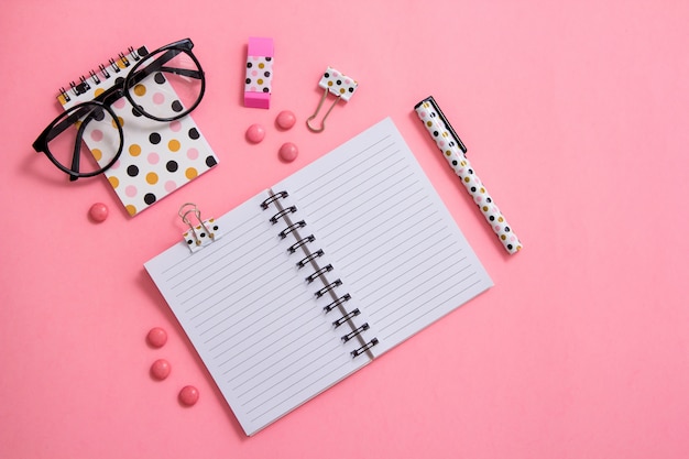 Bloc-notes, stylo et lunettes sur fond rose