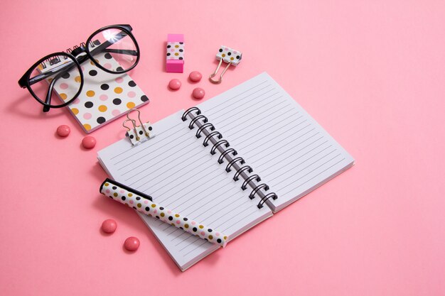 Bloc-notes, stylo et lunettes sur fond rose