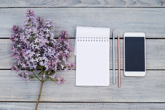 Bloc-notes, téléphone et branche lilas sur la table en bois blanche