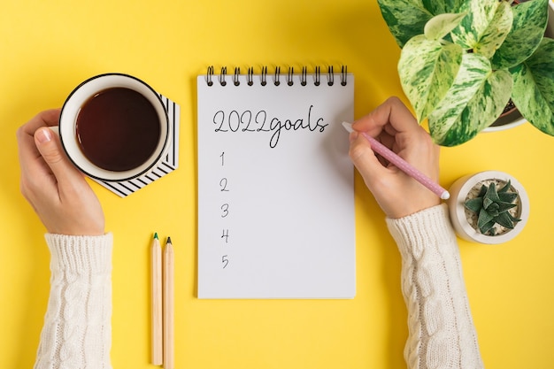 Bloc-notes vierge de bureau et mains de femme écrivant des plans et des objectifs texte à plat de la table de travail jaune