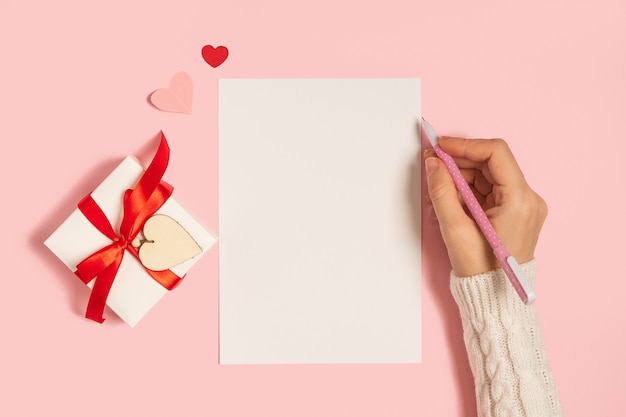 Bloc-notes vierge de bureau. Mise à plat de la main de la femme sur fond de table de travail rose avec cadeau Saint-Valentin