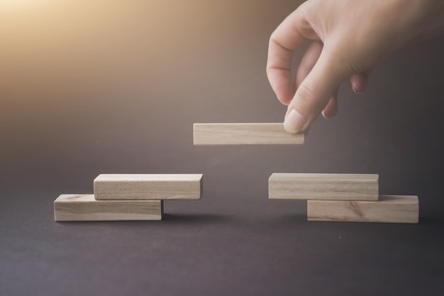 Blocs de bois s'empilant comme un escalier pyramidal sur fond marron. Création d'une organisation d'entreprise