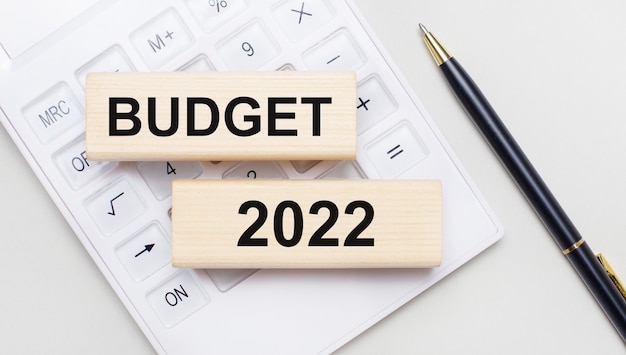 Des blocs de bois avec le texte BUDGET 2022 se trouvent sur un fond clair sur une calculatrice blanche. A proximité se trouve une poignée noire. Concept d'entreprise