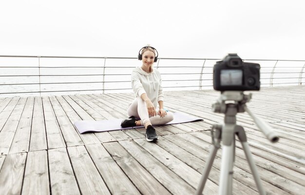 Blog de remise en forme. Jeune femme sportive en bonne santé s'enregistrant sur caméra avec trépied sur la plage. Vlogging