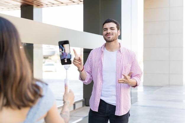 Blogger faisant des gestes pendant qu'un ami enregistre une vidéo sur un smartphone au centre commercial