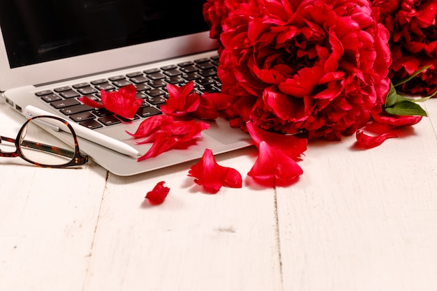 Blogger ou pigiste avec un ordinateur portable, un clavier, des pivoines rouges sur fond blanc