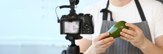 Le blogueur chef tenant un avocado donne des conseils de cuisine pour le vlog à la maison