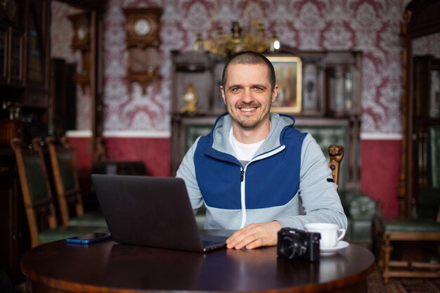 Blogueur indépendant homme regardant à huis clos et souriant assis dans un intérieur vintage