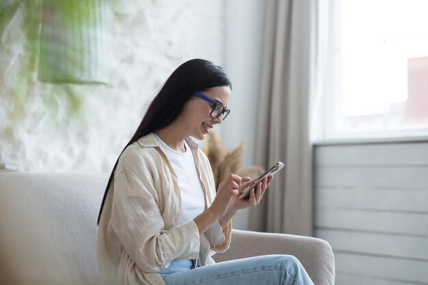 Un blogueur indépendant satisfait d'une belle jeune femme à lunettes assise à la maison sur le canapé près du