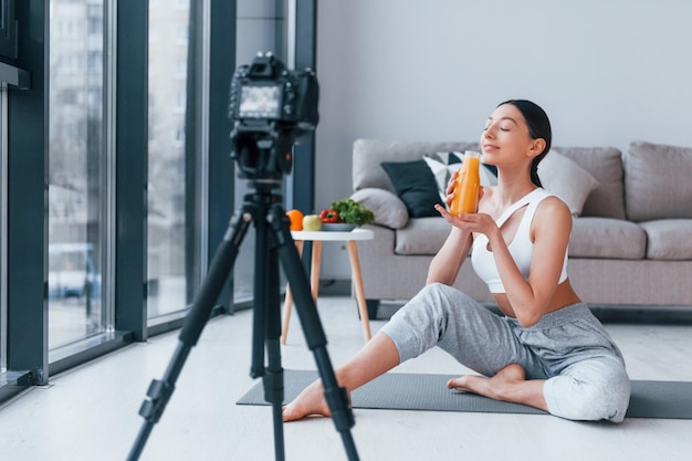 Blogueur jeune femme au corps mince en vêtements de sport parlant de légumes fruits et d'aliments sains à l'intérieur à la maison