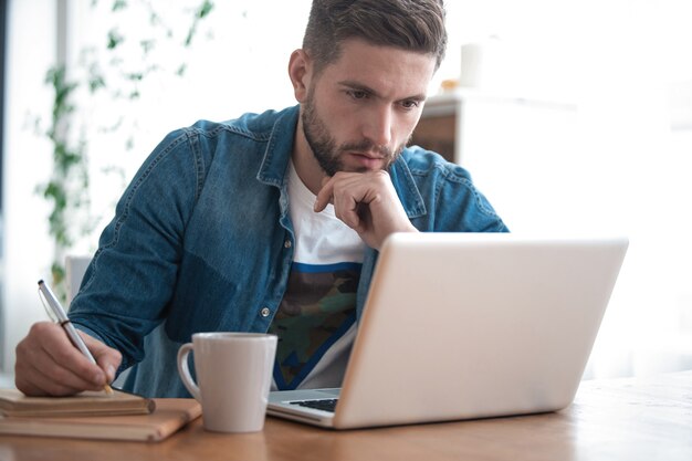 Blogueur joyeux. Bel homme moderne designer travaillant sur ordinateur portable en ligne, utilisant Internet à la maison