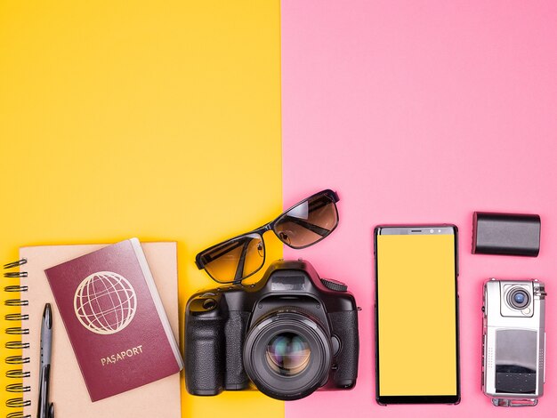 Blogueur prêt pour les voyages et les vacances d'été. Vue de dessus. Mise à plat. DSLR et caméra d'action, lunettes de soleil, smartphone et passeport sur fond bicolore. Couleurs pastel