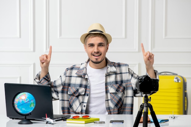 Blogueur de voyage beau jeune homme enregistrant un vlog de voyage sur caméra avec des bagages jaunes rêvant