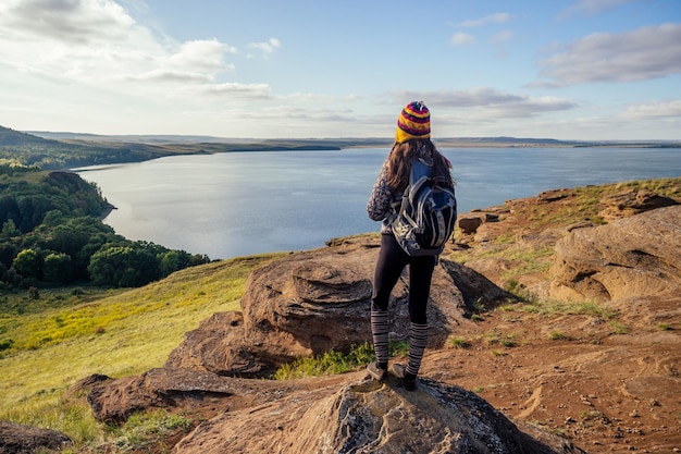 Blogueur de voyage femme dans un chapeau drôle du Népal Mountain Hiker avec randonnée sac à dos marchant sur d'énormes pierres orange paysage lac et collines