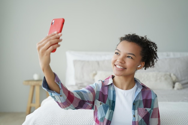 Une blogueuse adolescente de race mixte discutant en ligne par appel vidéo téléphonique à l'aide d'applications mobiles modernes à la maison