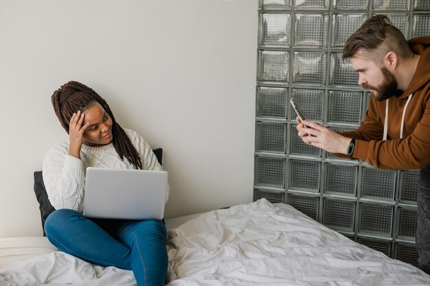 Une blogueuse afro-américaine joyeuse avec un ordinateur portable pendant qu'un gars fait des photos pour un blog ou des médias sociaux