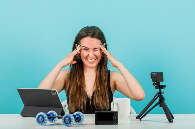 Une blogueuse amusante fait un clin d'œil à la caméra en se tenant la main sur les tempes sur fond bleu