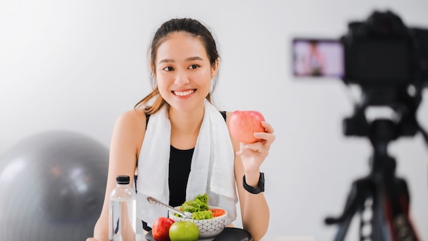 Une blogueuse asiatique en bonne santé montre des fruits et des aliments diététiques propres. Devant la caméra pour enregistrer des vidéos vlog en streaming à domicile.Fitness influenceur sur les réseaux sociaux en ligne.