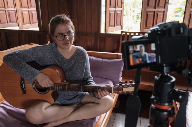 Blogueuse asiatique jouant de la guitare sur les réseaux sociaux. Concept de cours en ligne de guitariste tout en restant à la maison