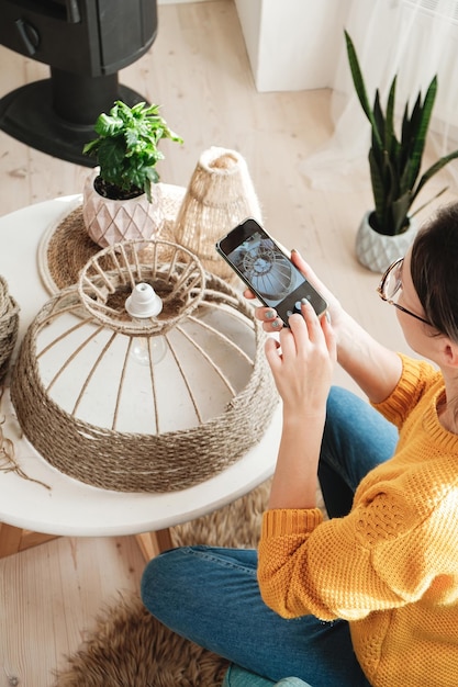 Une blogueuse de bricolage prend une photo sur un téléphone portable pour un blog de bricolage dans les médias sociaux lampe de corde de jute faite à la main à la maison