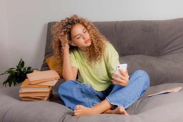 Une blogueuse avec un casque et un smartphone dans les mains est assise en tailleur sur un canapé gris