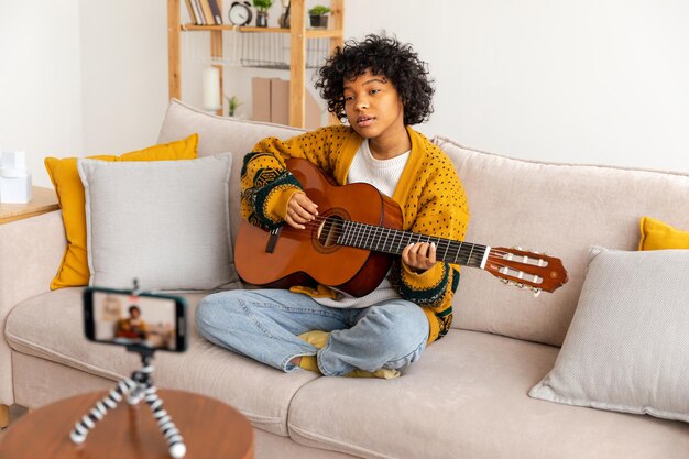 Blogueuse guitariste Afro-américaine fille blogueuse jouant de la guitare parlant à la webcam enregistrant vlog Femme influente des médias sociaux en streaming à la maison à l'intérieur Créateur de contenu musical tutoriel de diffusion