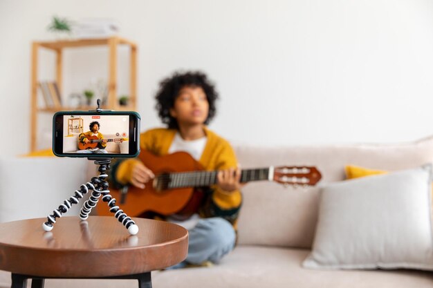 Blogueuse guitariste Afro-américaine fille blogueuse jouant de la guitare parlant à la webcam enregistrant vlog Femme influente des médias sociaux en streaming à la maison à l'intérieur Créateur de contenu musical tutoriel de diffusion